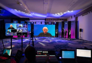 Hybrid event production setup with a large LED stage screen, cameras and control desks